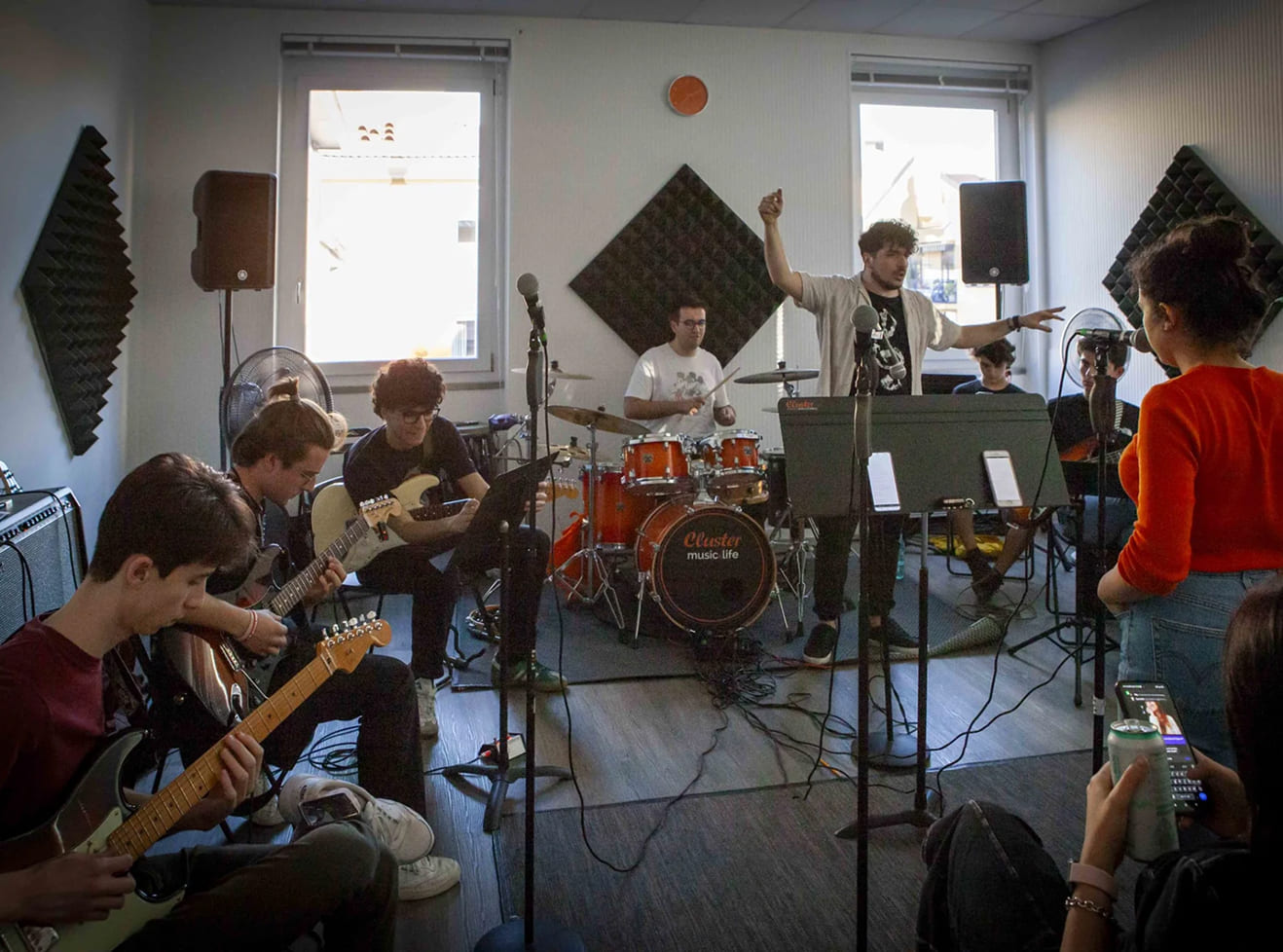 Lezione di Musica d’Insieme alla Scuola e Accademia di Musica Cluster con studenti che suonano chitarra elettrica, batteria e tastiera, guidati da un docente in aula attrezzata