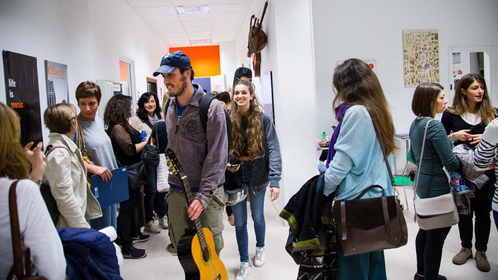 Studenti e visitatori accedono alla Scuola e Accademia di Musica Cluster per l’Open Day, accolti in un ambiente informale e sorridente, con chitarre in mano e staff presente