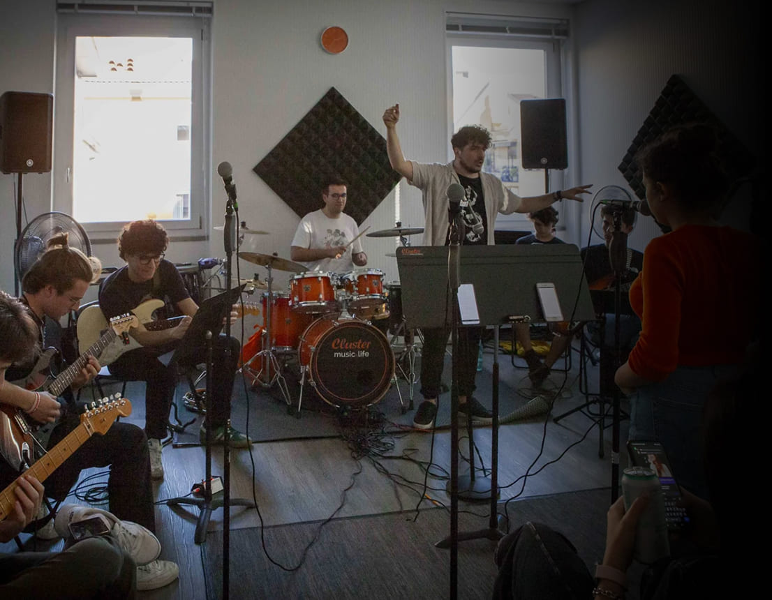 Lezione collettiva di Musica d'Insieme alla Scuola e Accademia di Musica Cluster con studenti che suonano chitarra elettrica, batteria e tastiera, accompagnati da un insegnante