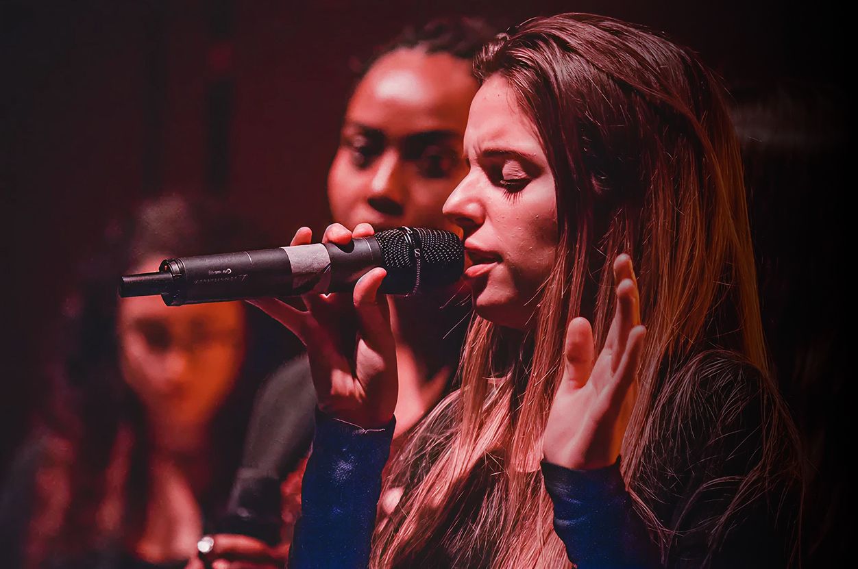 Studentessa canta al microfono durante una lezione di canto alla Scuola e Accademia di Musica Cluster, accompagnata da altre allieve